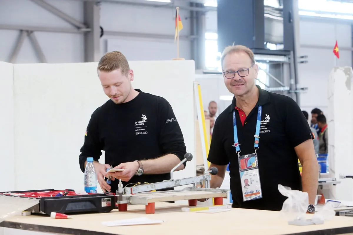 Fliesenleger Janis Gentner legt mit seiner Aufgabe los. Trainer Roland Filkorn unterstützt ihn, wo er nur kann und darf.