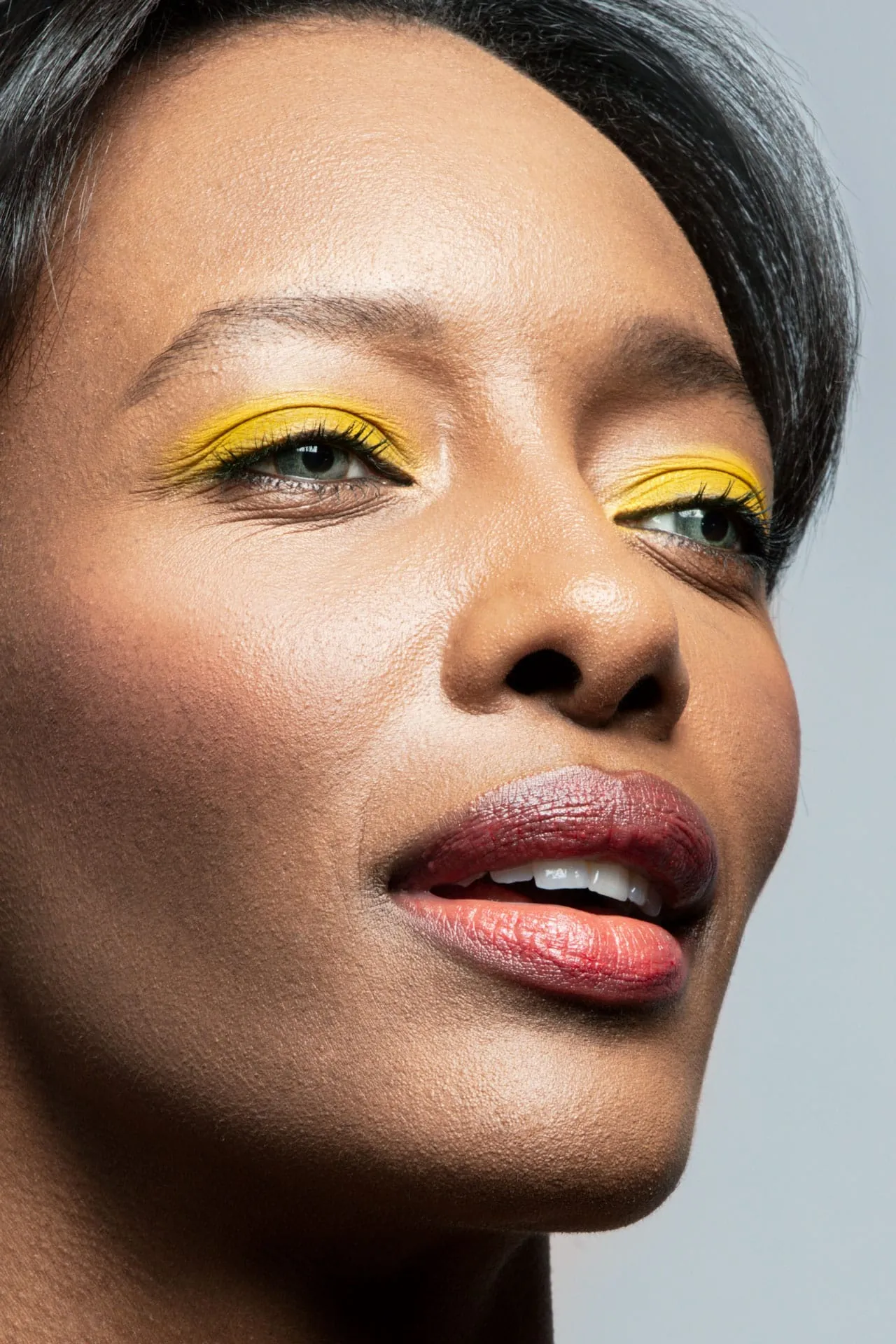 Beauty Look: Summer Vibes (Serie F1) Zitonengelb leuchtet es in diesem Sommer von den Augenlidern. Im ersten Schritt wird eine Grundierung aufgetragen, die mit einem Bronzer fixiert wird. Den Augenbrauen schenkt eine Cremecolor mehr Fülle und Schwung. Das bewegliche Lid wird mit zitronengelbem Puderlidschatten ausgefüllt und nach oben und unten verblendet. Um den Augen mehr Ausdruck zu verleihen, wird auf der oberen und unteren Wasserlinie schwarzer Kajal aufgetragen. Zusätzlich verstärkt schwarzer Kajal zwischen den Wimpern die Wirkung. Anschließend werden die Wimpern komplett mit schwarzer Mascara getuscht. Für ein frisches Finish wird ein roséfarbenes Rouge auf die Wangenknochen aufgetragen. Für betonte Lippen eignet sich ein rostroter Lippenstift.