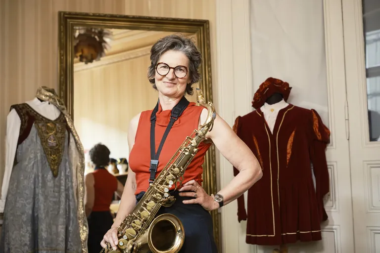 Zwischen Karneval und Handwerk: Die Schneidermeisterin mit ihrem Saxophon zwischen den Kostümen.