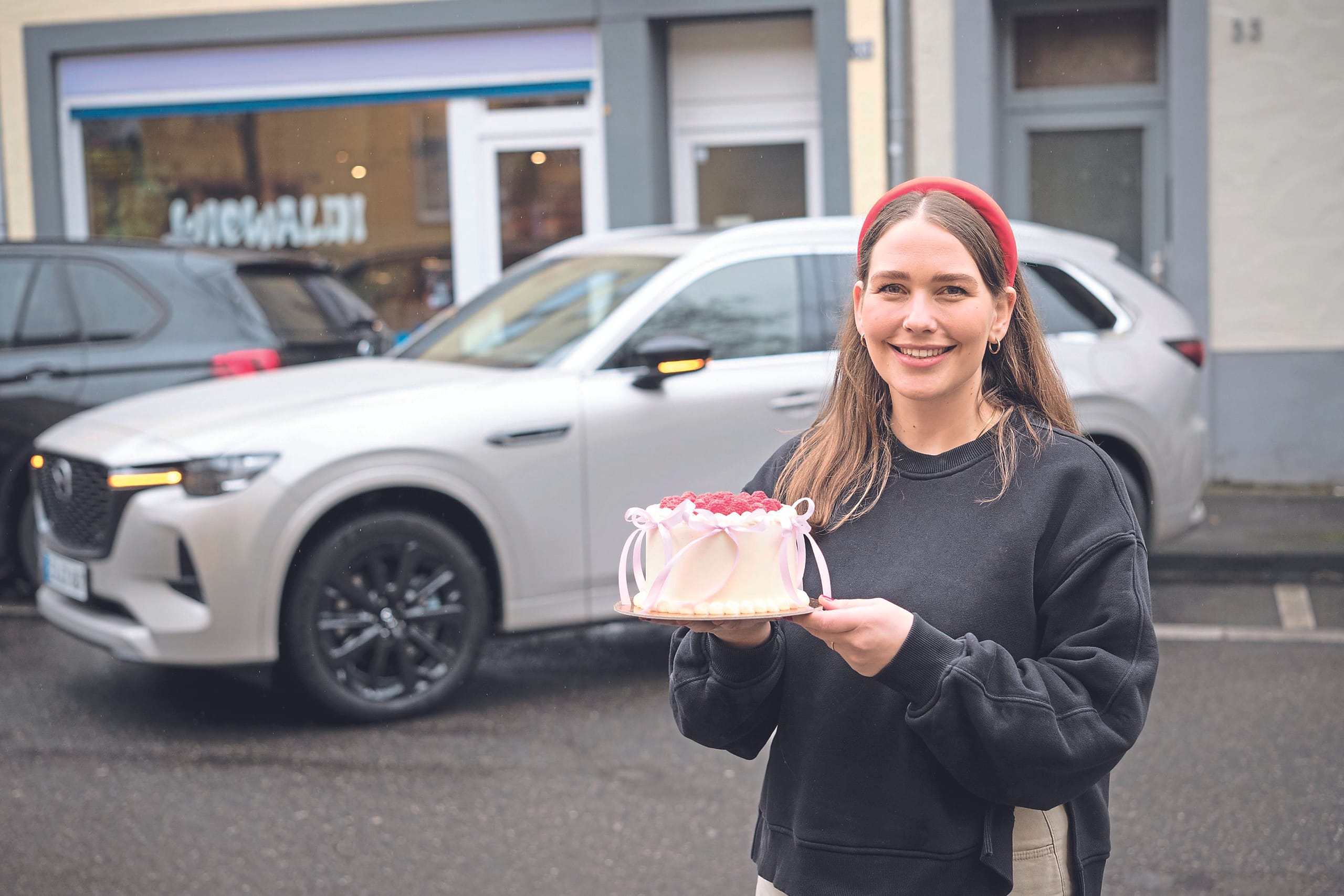 Das Tortenmobil: Konditorin Pola Held testet den weißen Mazda CX-80, der farblich bestens auf ihre Torte abgestimmt ist.