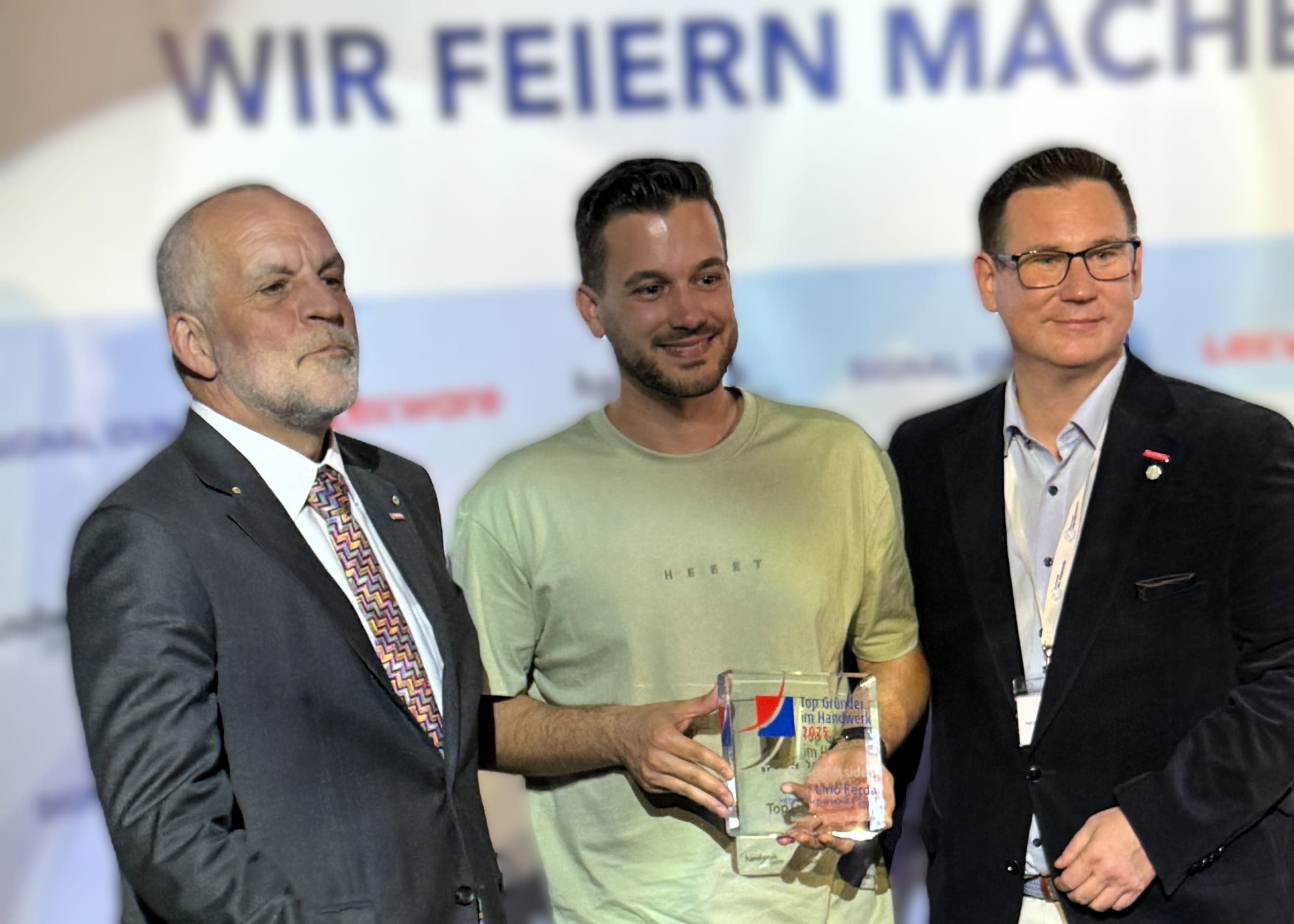 Und jetzt nochmal offizielle Siegerbilder vor der Logowand: Den Anfang macht Lino Ferda, der für seine „Top Geschäftsidee“ geehrt wurde. Umrahmt wird er hier von Markus Renfordt (li.), Präsident der Handwerkskammer Südwestfalen, in der HEET heimisch ist, und Kay Schlüter (re.), Abteilungsleiter Betriebsberatung des Kammerbezirks.