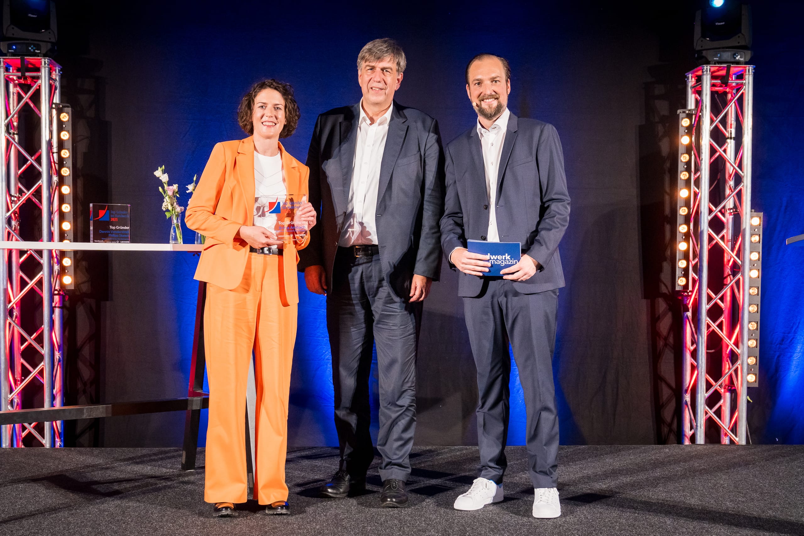 „Top Gründerin“ 2025 ist Britta Ambach (li.), Gründerin des gleichnamigen Musikhauses in Winnenden. Mit ihr freuen sich Laudator Jan Peter Kruse und Moderator Patrick Neumann (re.).